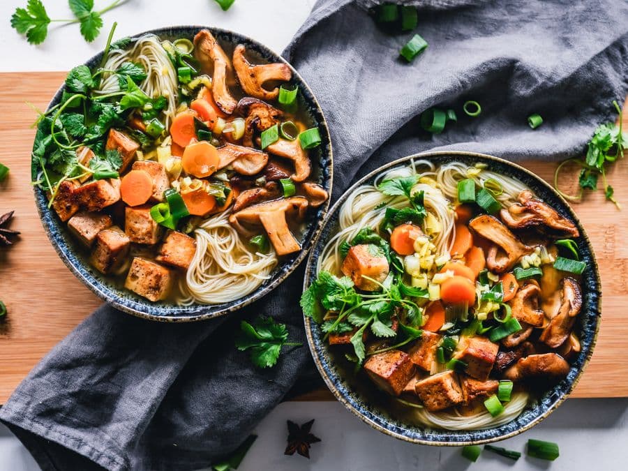Two bowls of noodle soup with crispy tofu, mushrooms, carrots and fresh coriander