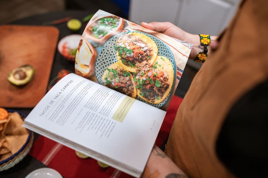 Hands holding open a cookbook showing a taco recipe across two pages