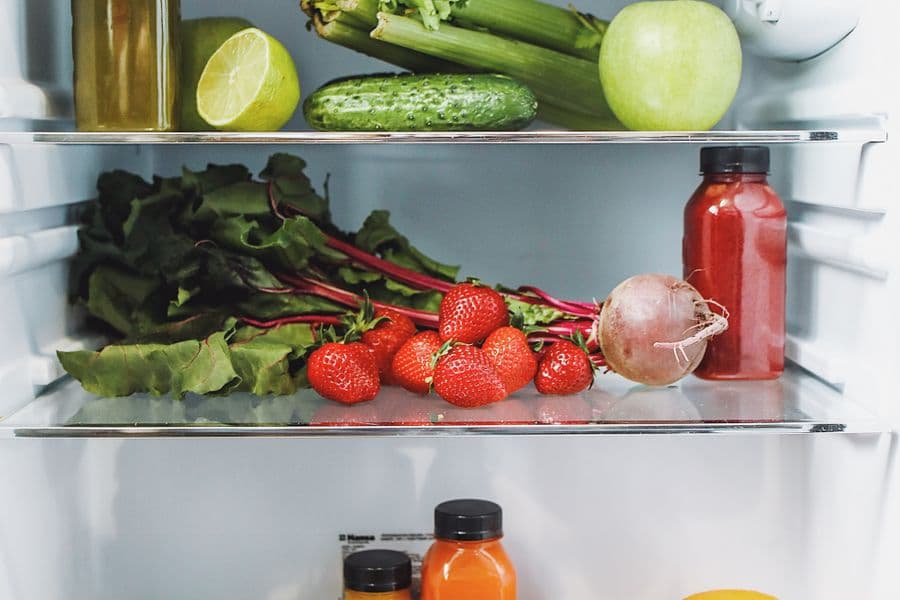 An open fridge stocked with colourful vegetables, fruit and juices