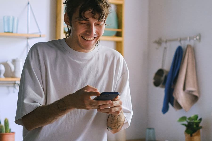 A smiling man checking his phone in a bright home kitchen